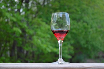 Wine glass and red wine on the wood railing with a green tree background