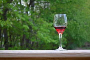 Wine glass and red wine on the wood railing with a green tree background