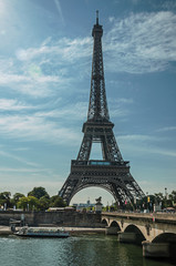 Tourist boat over Seine River, bridge and stunning Eiffel Tower in a sunny blue sky at Paris. Known as the “City of Light”, is one of the most impressive world’s cultural center. Northern France.