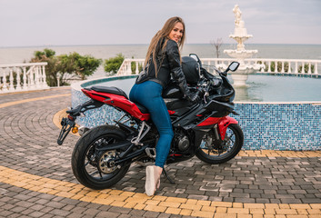 Fototapeta na wymiar Biker girl in a leather jacket on a black and red color motorcycle.