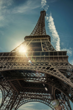 Bottom view of Eiffel Tower made in iron, with sunny blue sky in Paris. Known as the “City of Light”, is one of the most impressive world’s cultural center. Northern France. Retouched photo