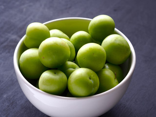 green fresh plums in white bowl with black wood background