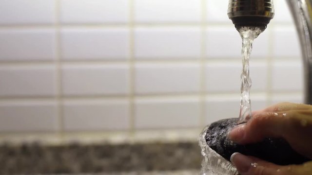 Close-up of female hand washing a raw mussel under running water in sink. Preparation of mussels before the cooking. Slow motion.