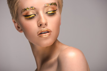 attractive woman with golden shiny makeup looking down isolated on grey