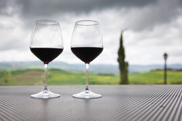 two glasses of red wine against beautiful landscape in Tuscany