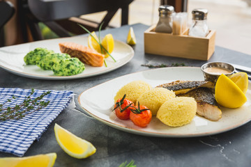 Fish dishes with millet porridge, tomato, lemon slice and shrimp sauce on dark table