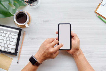 Man using mobile phone on office white wooden desk table with computer , office supplies and coffee cup.