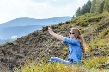 Young girl in blue clothes, wearing sunglasses doing selfie in summer outdoors