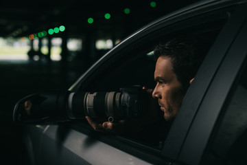 side view of male paparazzi doing surveillance with camera from his car