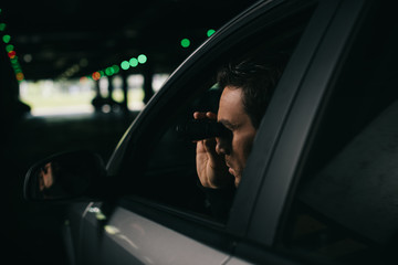 male paparazzi doing surveillance by binoculars from car