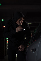 Obraz na płótnie Canvas male robber in black hoodie with flashlight looking into car