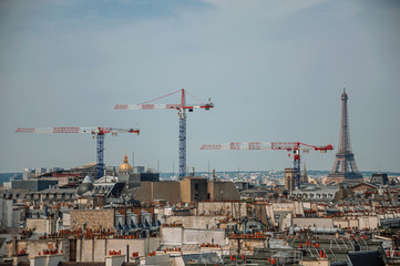 Fototapeta na wymiar Close-up of buildings rooftops, cranes and Eiffel Tower on the horizon in Paris. Known as the “City of Light”, is one of the most impressive world’s cultural center. Northern France. 