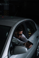 high angle view of male undercover agent in sunglasses aiming by gun from car
