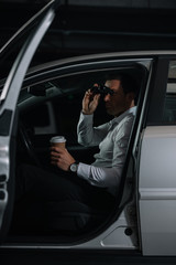 undercover male agent spying by binoculars and drinking coffee in car