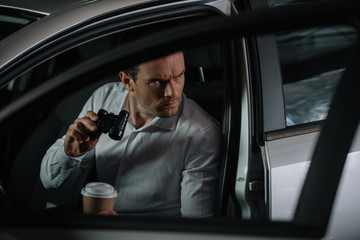 concentrated undercover male agent doing surveillance by binoculars and drinking coffee in ca