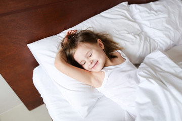 Little girl sleeping in morning before school on bed with white linens. Concept of childhood and resting.