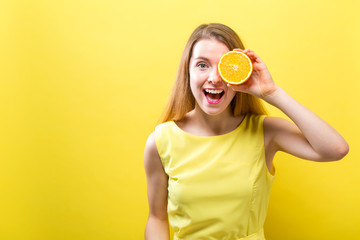 Happy young woman holding a half orange on a yellow background