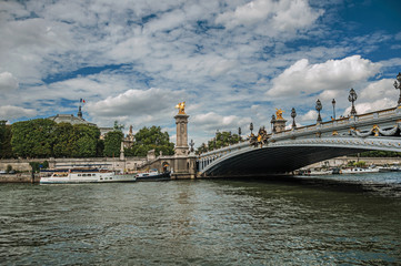 Fototapeta na wymiar Alexandre III bridge, Grand Palais building and boats anchored at Seine River bank in Paris. Known as the “City of Light”, is one of the most impressive world’s cultural center. Northern France.