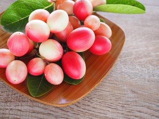 Carissa carandas or karonda are white and red with green leaves in wooden plates. On the old wood table It is a small fruit and has medicinal properties. Vitamin C is high when cooked to sour taste.