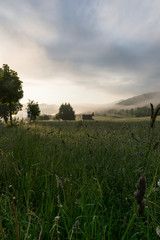 Misty mountains, early hazy morning over a mountain meadow or a field with green forested hills, Krasno polje village near Velebit mountain national park in Croatia