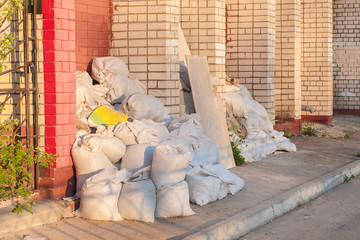 construction waste in white construction bags lie on the street near the brick wall