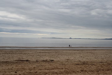 Fototapeta na wymiar Two people walking on a beach on a cloudy day