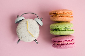 Flat lay of colorful macarons on pastel pink background. One of them in shape of alarm clock.