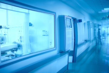 Hospital building hallway with observation window to the ward and blurred silhouette of a female worker