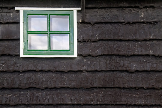 Brown wooden wall with small window in white frame, typically Netherlands house architecture fragment