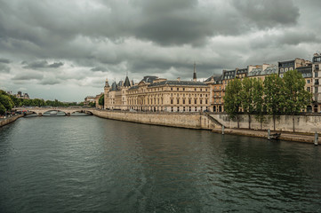 Old buildings, promenade with lined trees on the bank of Seine River and cloudy sky in Paris. Known as the “City of Light”, is one of the most impressive world’s cultural center. Northern France.