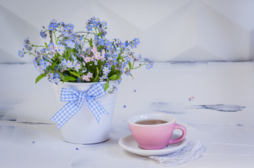 Bouquet of forget-me-nots in metal bucket and and cup of tea on white background. Place for text.