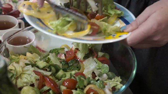 Woman putting fresh vegetable salad from bowl to plate.