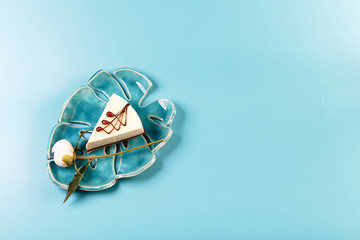 Picturesque still life in blue tones, decorative plate with piece of cheese cake surrounded by white pions, flower bud, blue background, copy space, top view, set
