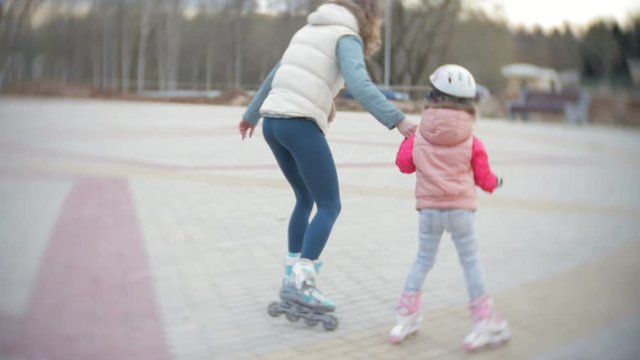 Mom and daughter ride on roller skates. Girl learning to roller skate, and falls. Mom teaches daughter to ride on rollers