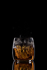 A glass of whiskey with ice cubes on a black background. Spray of whiskey.