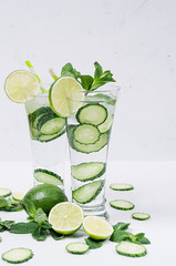 Summer cold detox water with slices cucumber decorated pieces lime and mint on white wood board.