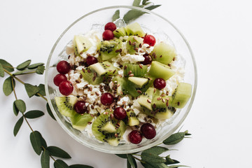 Delicious cottage cheese with kiwi pieces and cranberries in bowl on white background, closeup, healthy breakfas