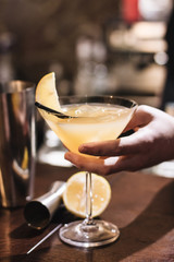 Woman holding delicious cocktail with ice cubes, lemon and straws in bar