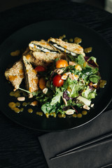 Fresh green salad with crackers on black plate