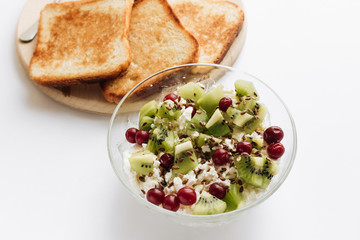 Delicious cottage cheese with kiwi pieces and cranberries in bowl and toasts on white background, closeup, healthy breakfast