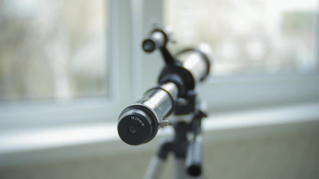 A little girl looks through a telescope from the window of her house