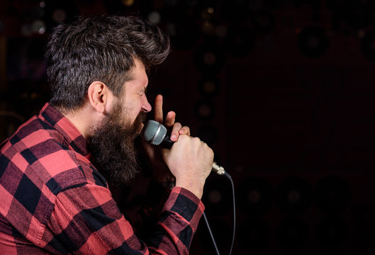 Talented vocalist concept. Man on tense face holds microphone, singing song, black background, copy space. Musician, vocalist with beard and mustache lighted by spotlight.