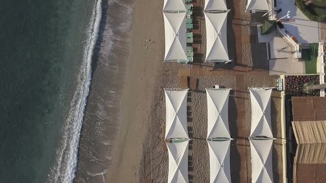 Aerial footage of coast line with umbrellas on sandy beach. Bird eye view