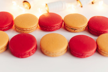 stylish colorful red and yellow macaroons stacked on white background with christmas lights. space for text. catering for celebrations and holidays concept