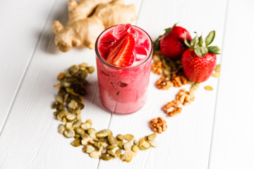 A strawberry ginger smoothie cocktail in a highball glass, garnished with fresh berries, ginger, walnuts and pumpkin seeds. White wooden table.