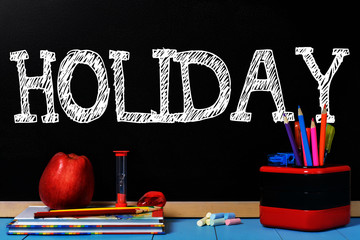 Text Holiday on black chalkboard with school accessories