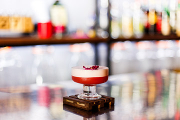 A lifestyle photo of a clover club alcoholic drink in a cocktail glass, served on a small wooden board, standing on a steel barstand. Selective focus, grain effect, bokeh background.