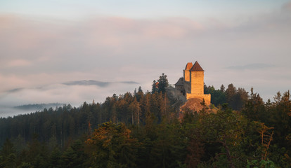 Obraz premium Sunrise in Kasperk castle, Sumava, Czech Republic. Hills and villages in the fog, misty view on Czech landscape, evening scene.