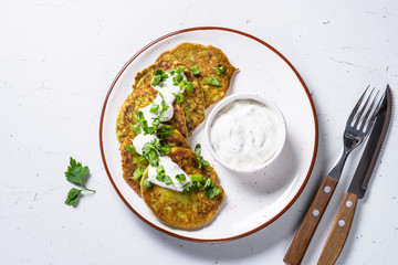 Zucchini pancakes with greens and sour cream on white.