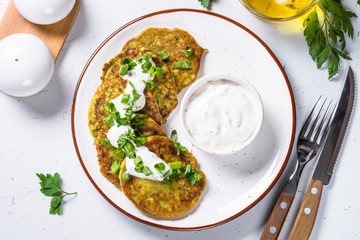 Zucchini pancakes with greens and sour cream on white.
